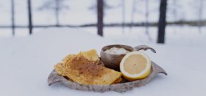 Lumihangella lautanen, jossa kikherne-leipä, sitruunan puolikas ja kuppi täynnä keittoa.
