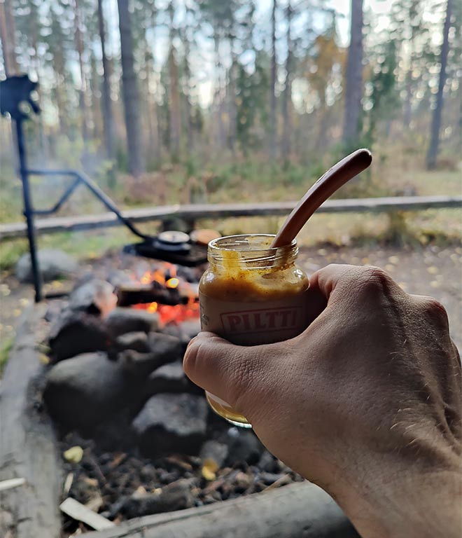 Pilttipurkki miehen kädessä ja nuotio näkyy taustalla