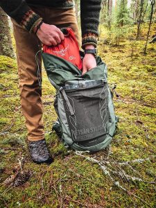 Henkilö pakkaa punaista pakkauksta Osprey Talon 33 -reppuun metsäisessä maastossa.
