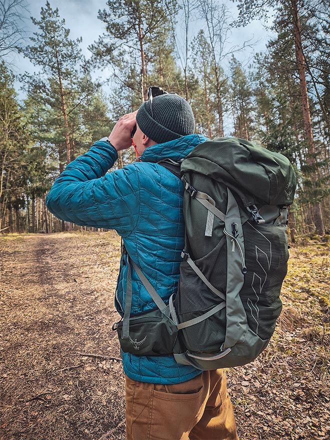 Henkilö katselee kiikareilla metsämaisemaa, Osprey Talon 33 -reppu selässä.