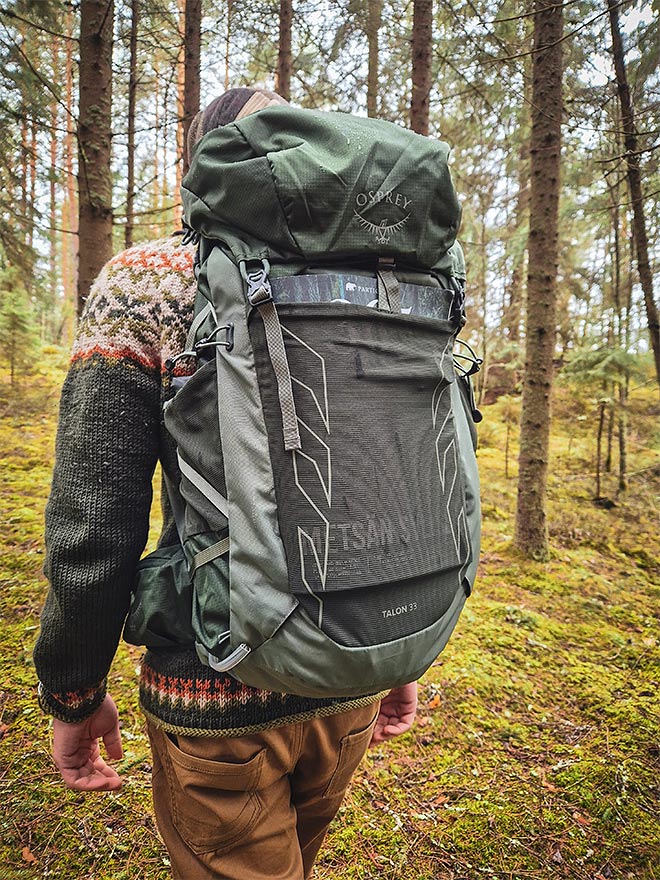 Henkilö kävelee metsässä vihreä Osprey Talon 33 -reppu selässään.