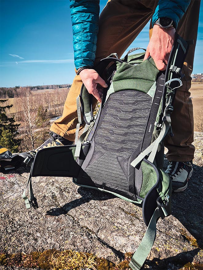 Henkilö esittelee Osprey Talon 33 -repun ilmastoitua selkäpaneelia kalliolla.