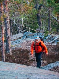 Retkeilijä kulkee metsäpolkua ylämäkeen kohti kalliota, taustalla näkyy puiset portaat ja metsäistä maastoa.