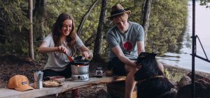 Nainen ja mies valmistavat retkiruokaa Trangialla. Taustalla metsämaisema.