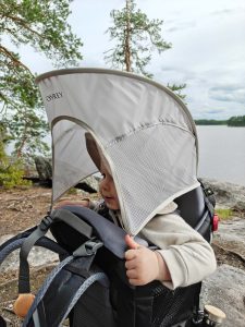 Lapsi istuu lastenkantorinkassa aurinkosuojan alla järven rannalla.