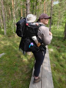 Aikuinen kantaa lasta lastenkantorinkassa pitkospuilla mäntymetsässä.