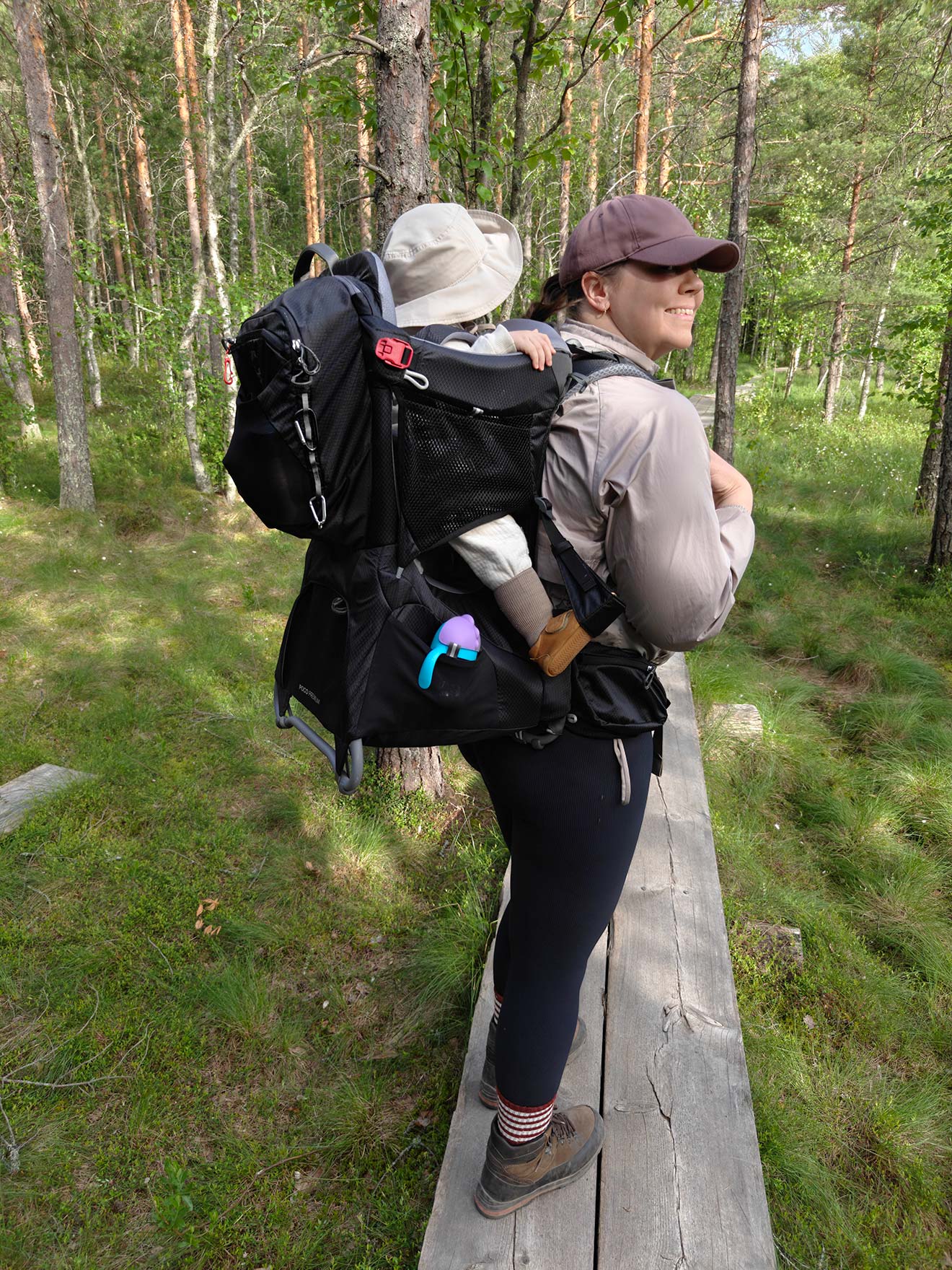 Aikuinen kantaa lasta lastenkantorinkassa pitkospuilla mäntymetsässä.