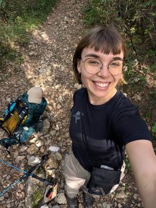 Retkeilijä ottaa selfien kivisellä metsäpolulla repun ja vaellussauvojen vieressä.