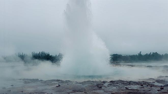 geysir purkautuu korkealle ilmaan höyryävän kuuman lähteen keskeltä islannissa.