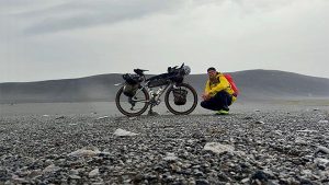 pyöräilijä kyykistyy lastatun bikepacking-pyörän vierelle karulla islannin ylängöllä.