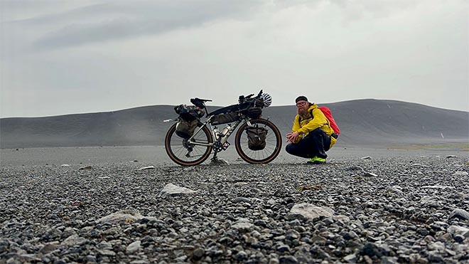pyöräilijä kyykistyy lastatun bikepacking-pyörän vierelle karulla islannin ylängöllä.