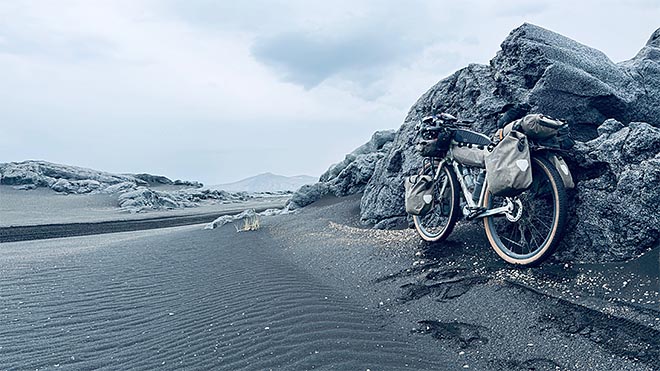 lastattu bikepacking-pyörä mustalla hiekalla laavakivien vieressä islannin ylängöllä.