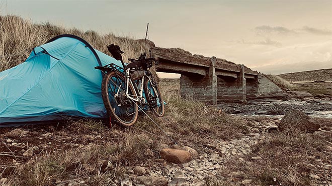 sininen teltta ja bikepacking-pyörä vanhan rakennelman vieressä islannin maaseudulla.