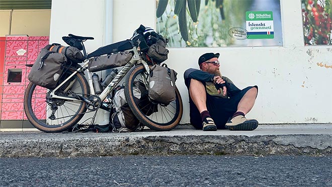 pyöräilijä istuu lastatun bikepacking-pyöränsä vieressä tauolla islannissa.