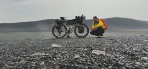 pyöräilijä kyykistyy lastatun bikepacking-pyörän vierelle karulla islannin ylängöllä.
