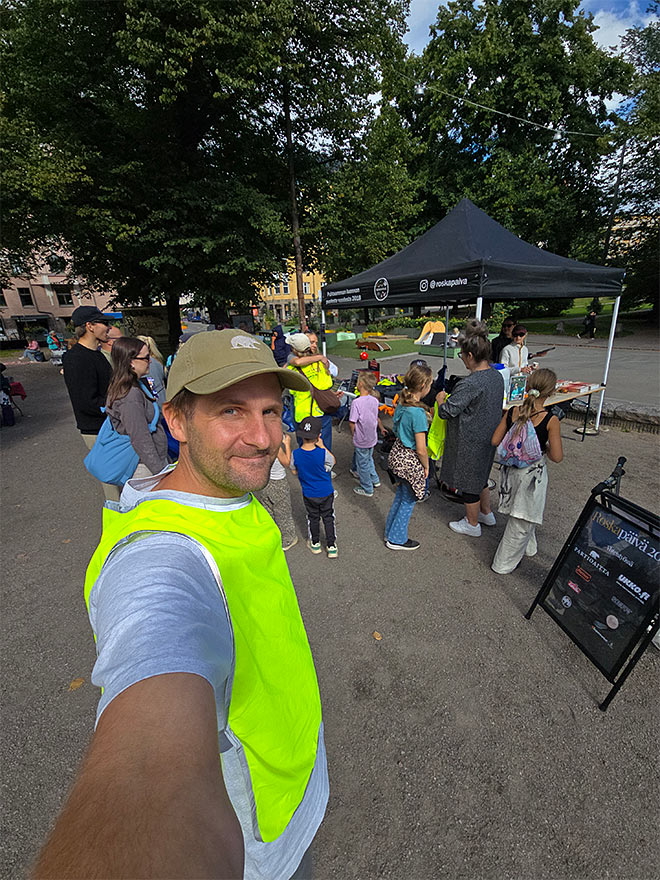 Mies ottaa selfien Roskapäivä-tapahtumassa, jossa osallistujia on kokoontunut teltan ympärille.